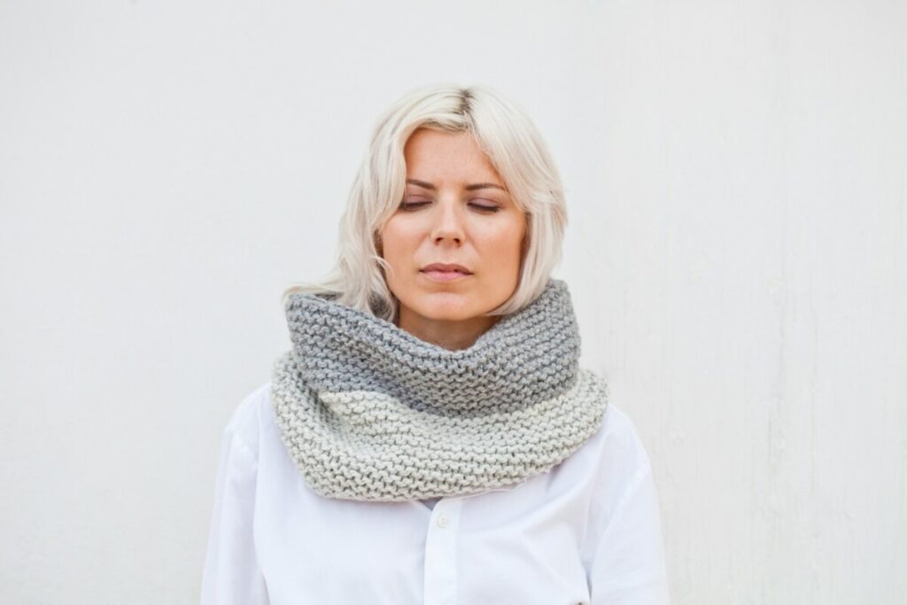 A woman in a white shirt is wearing a gray scarf