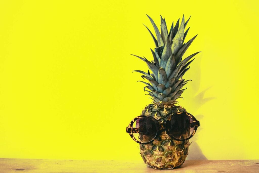 A stylish pineapple wearing sunglasses against a bright yellow background.