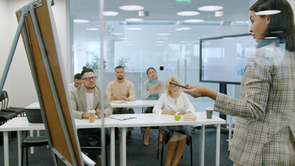Managers men and women are listening to employee young lady making report in conference room talking and gesturing using flipchart whiteboard.